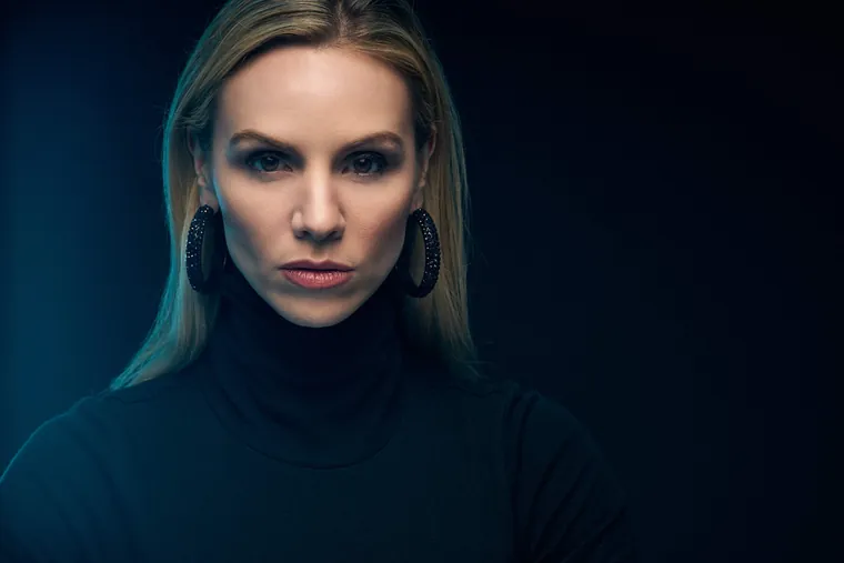 Cinematic actor headshot of a woman in a black turtleneck with large hoop earrings, lit in teal against a dark background
