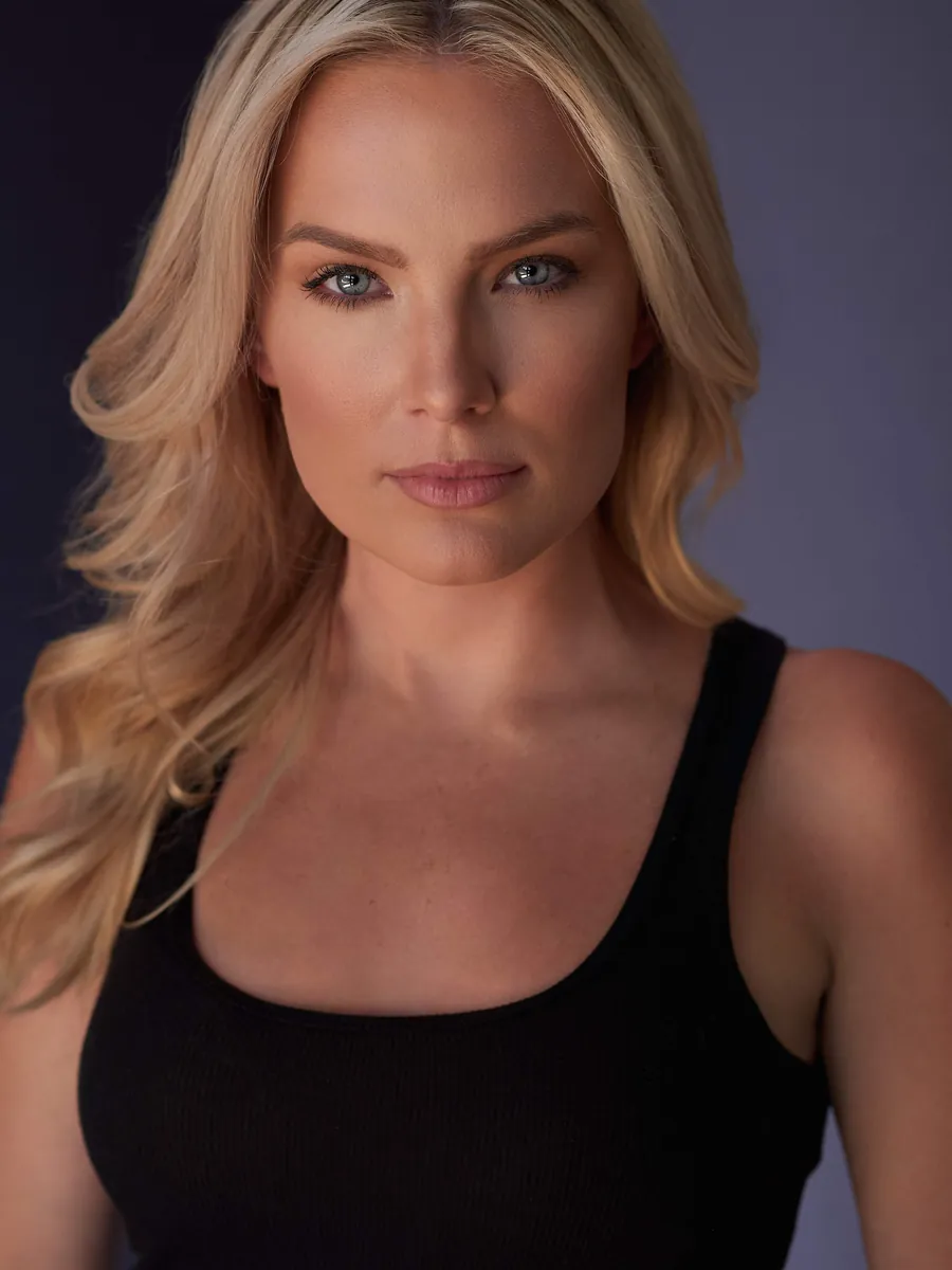 Actor headshot of a blonde woman in a black tank top against a soft purple-gray background