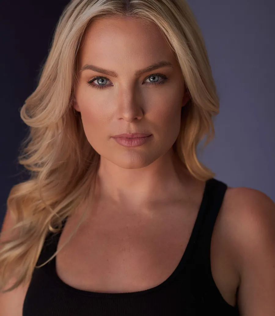 Actor headshot of a blonde woman in a black tank top against a soft purple-gray background