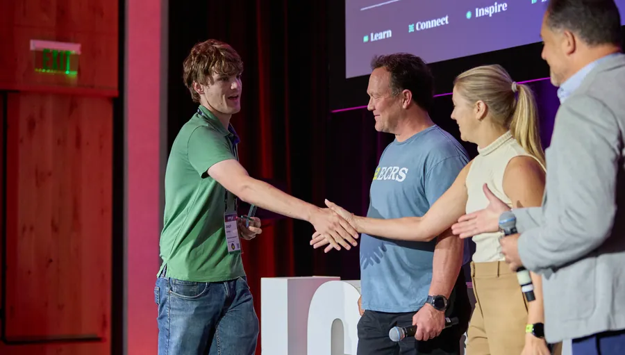 Award winner shaking hands with presenters on stage at ECRS Ignite 2026