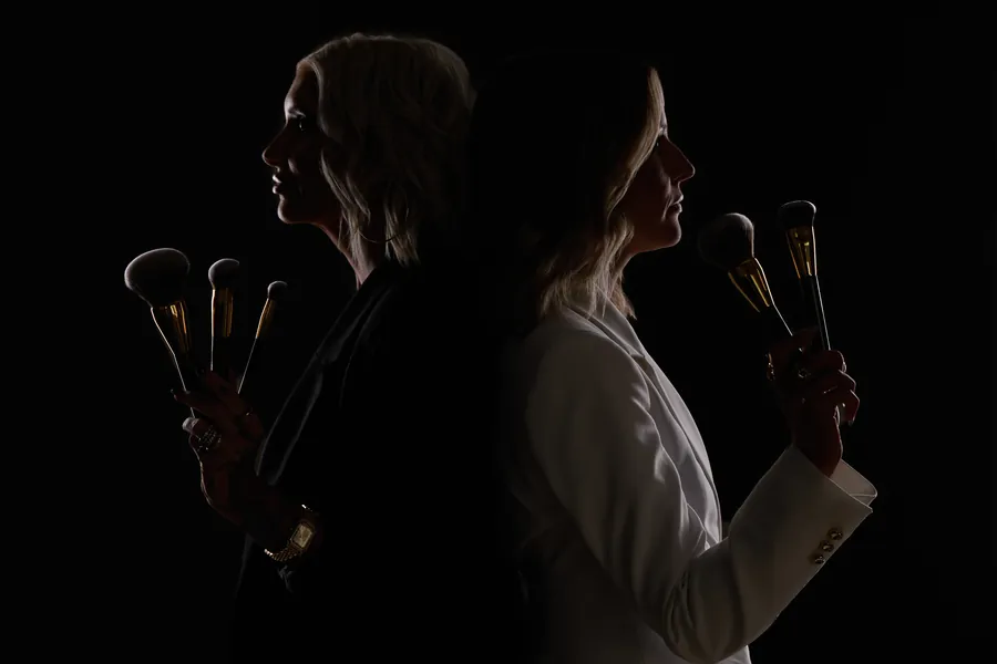 Backlit silhouette portrait of the two High Contrast Beauty founders standing back to back, holding makeup brushes