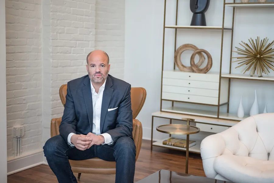 Bald executive in a navy blazer seated in a modern styled office, environmental headshot