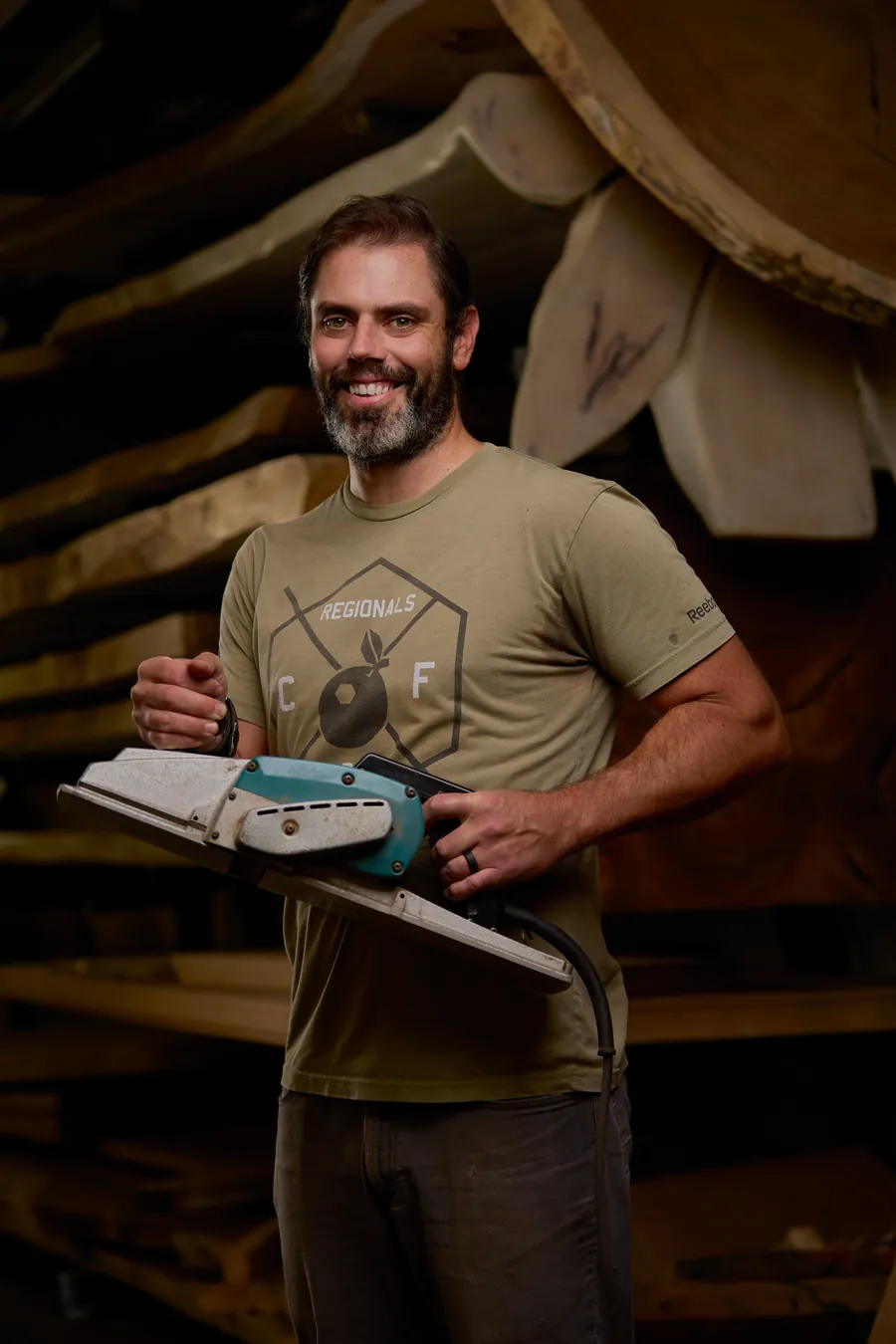Bearded man in an olive t-shirt holding a sander, branding portrait