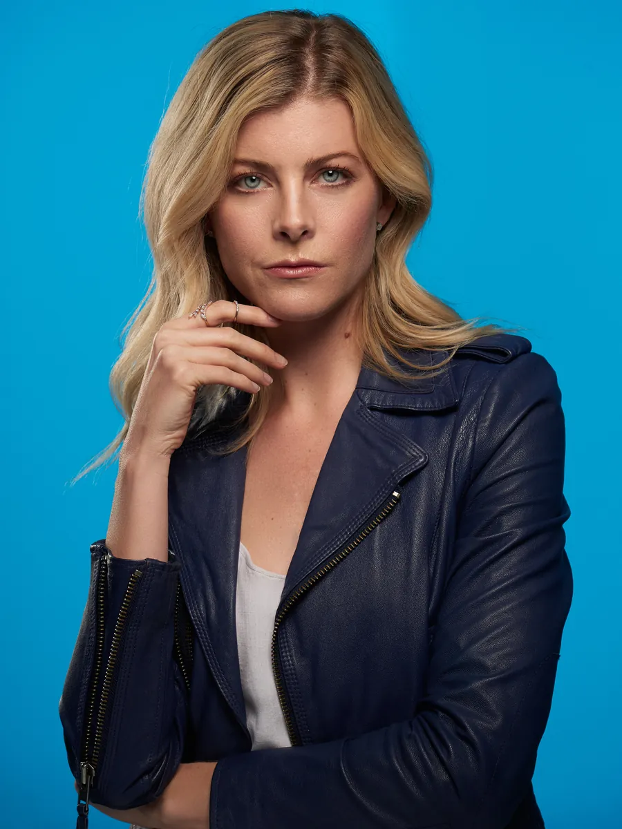 Blonde woman in a navy leather jacket against a bright blue background, professional headshot