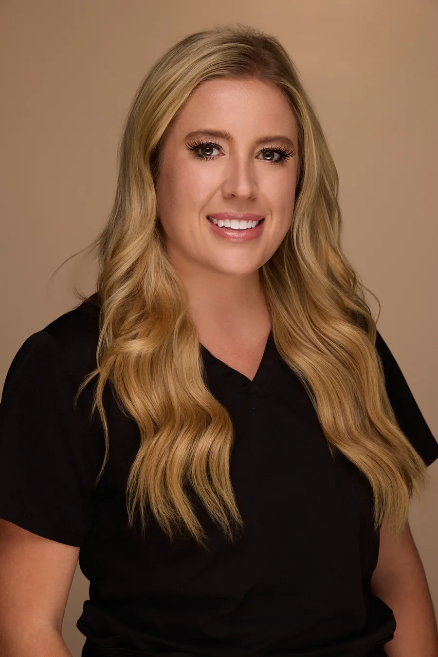 Blonde woman in black scrubs against a warm backdrop, team portrait