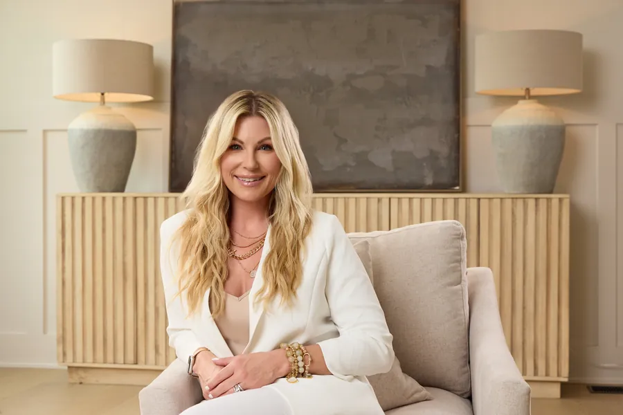 Blonde woman in cream seated in an armchair in a styled living room, brand portrait