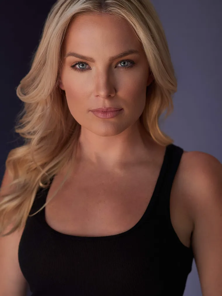 Character acting headshot of a blonde woman in a black tank top against a soft purple-gray background
