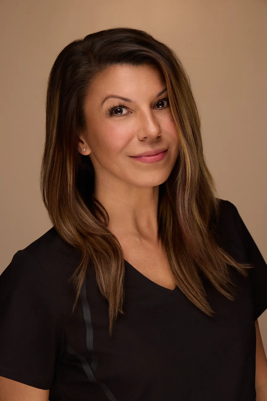 Dark-haired woman in a black top against a warm backdrop, team portrait
