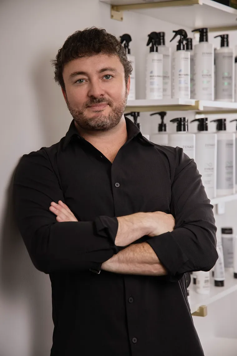 Man with arms crossed leaning against a wall of Zenagen product shelves, editorial headshot