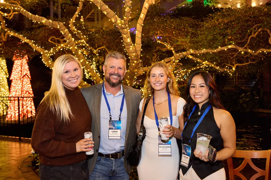 Four attendees with name badges smiling under string lights at a welcome reception