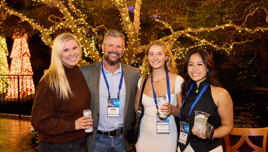 Four attendees with name badges smiling under string lights at a welcome reception