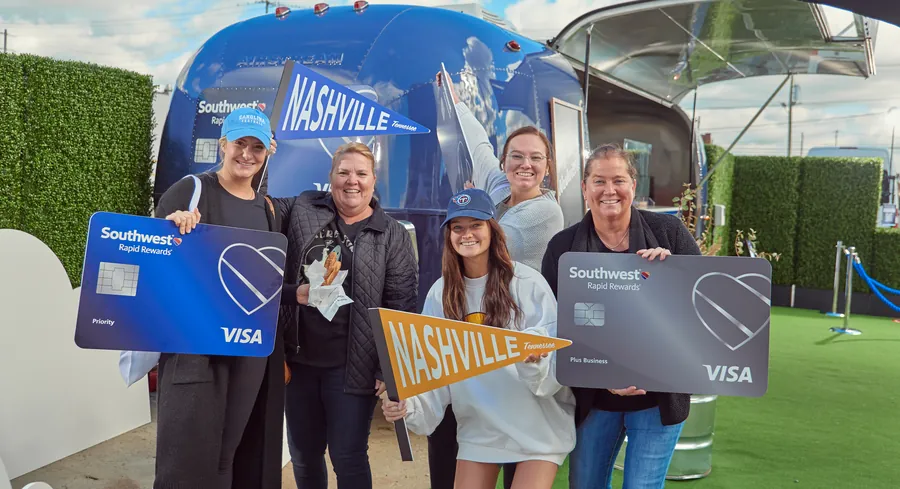 Group holding oversized cards in front of a Nashville-branded trailer at an outdoor brand activation