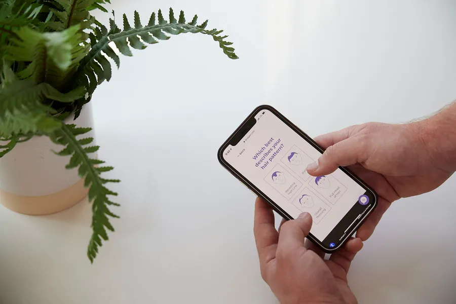 Hands holding a phone beside a fern, product photo from the Zenagen rebrand campaign