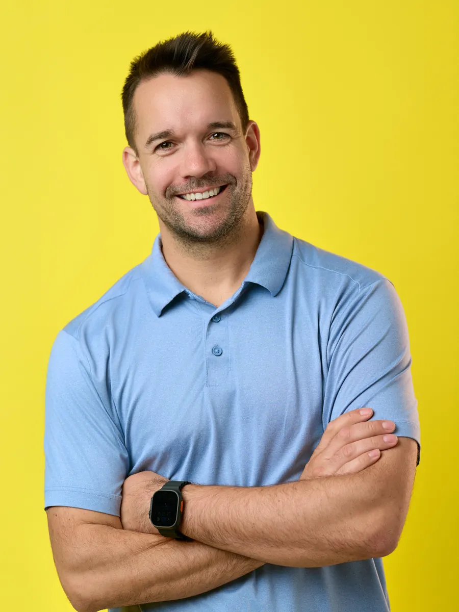 Jeff Carpenter, commercial photographer, smiling with arms crossed in a light blue polo against a yellow background