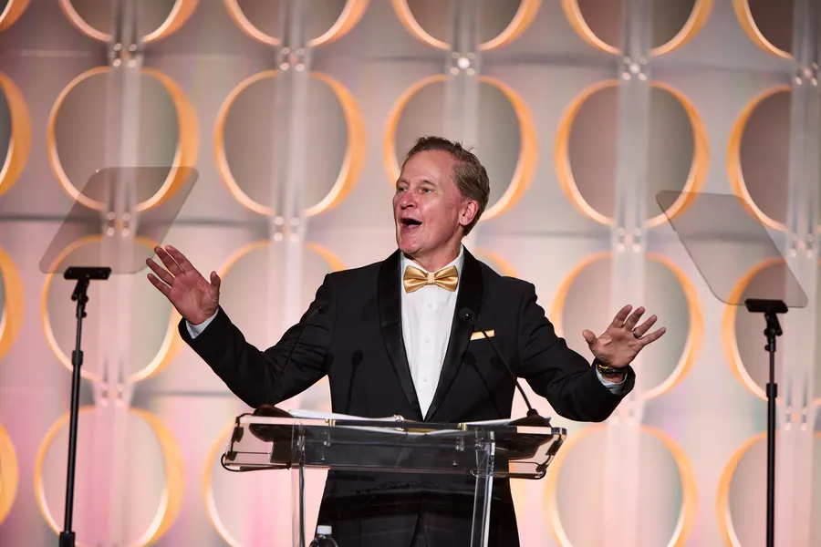 Man in a bow tie gesturing at a podium during an awards program