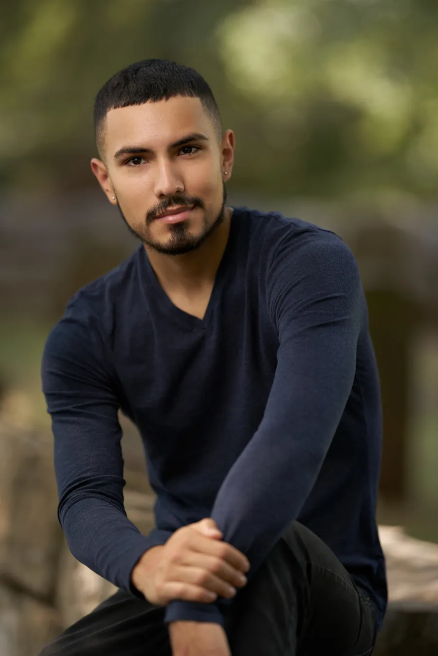 Man in a navy sweater crouching outdoors, lifestyle headshot