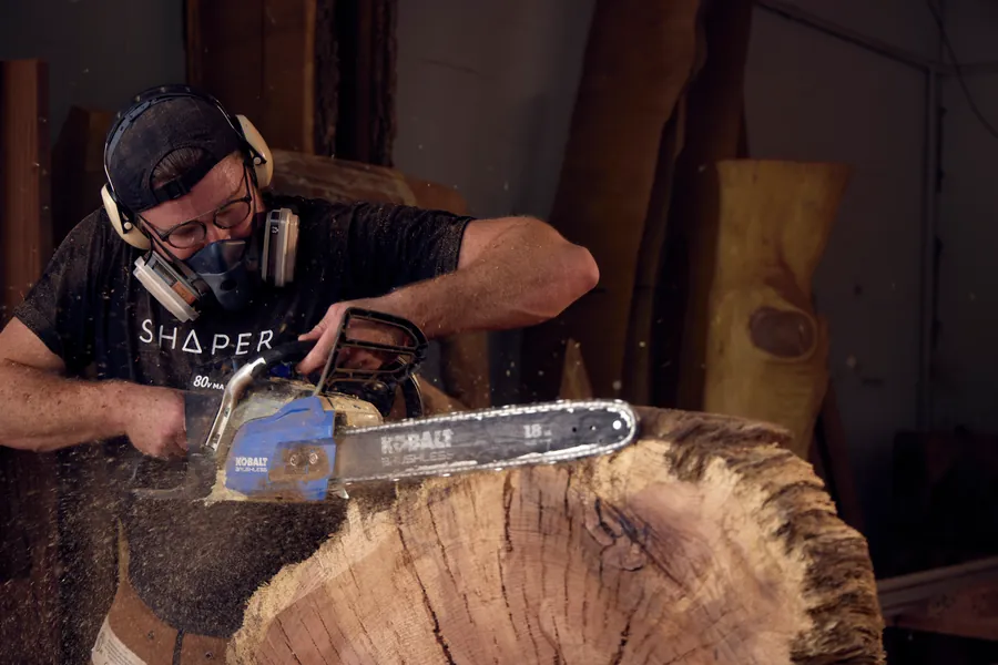 Man in safety gear cutting into a large log with a chainsaw, close-up action shot