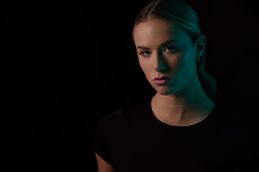 Moody actor headshot of a woman lit in teal against a black background
