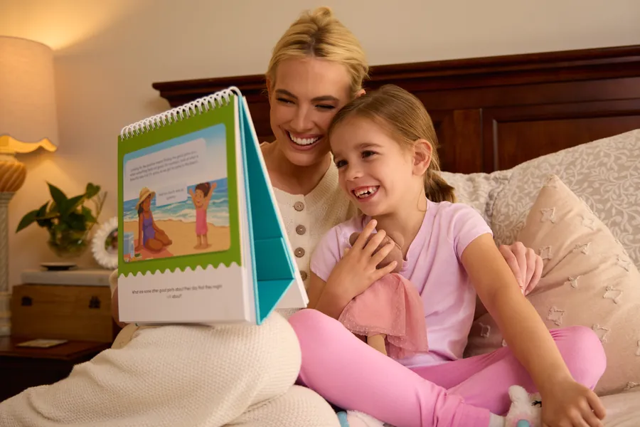 Mother and daughter laughing together while reading a Bright Pond activity book in bed