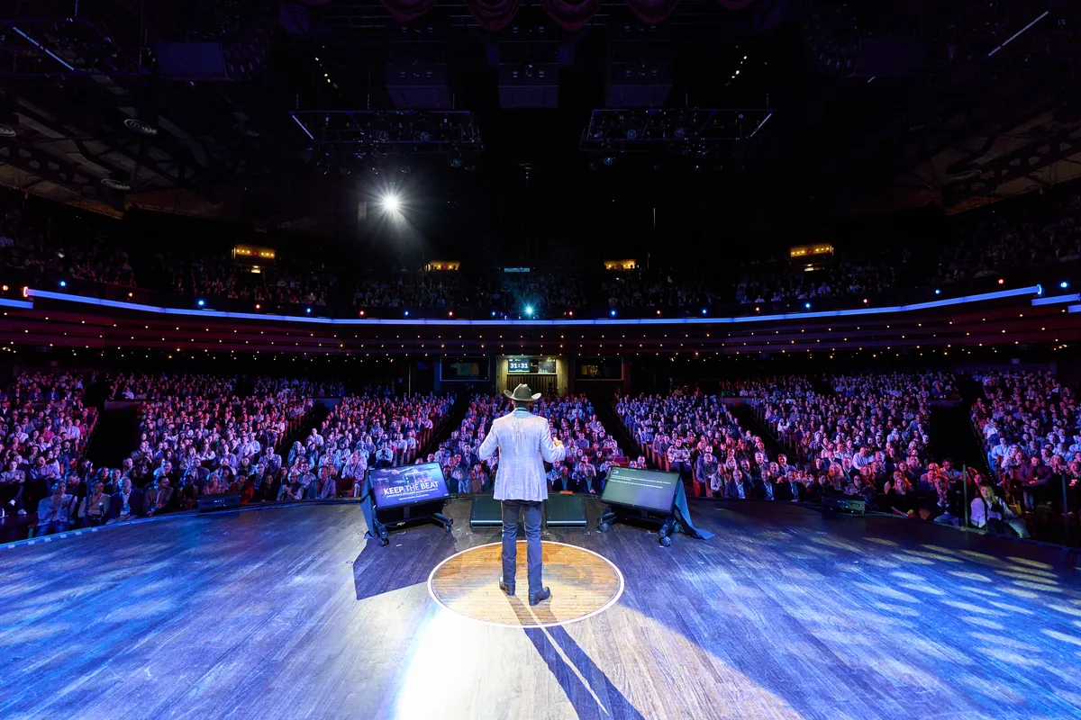 Speaker on a stage in front of a large arena audience at a Nashville corporate conference