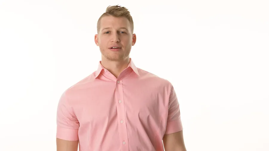On-camera bio video of a man in a pink shirt against a white studio backdrop — click to play