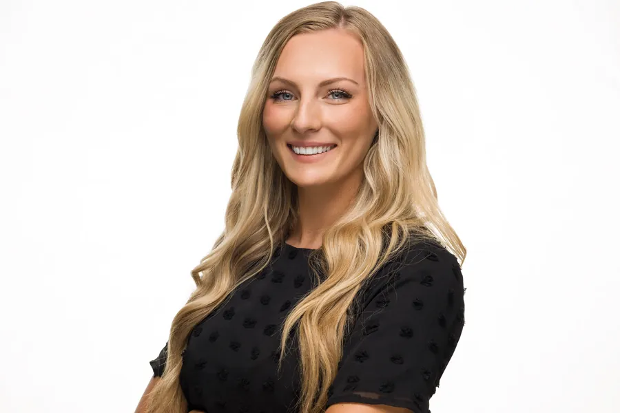 Smiling blonde woman in a black polka-dot top against a white background, headshot