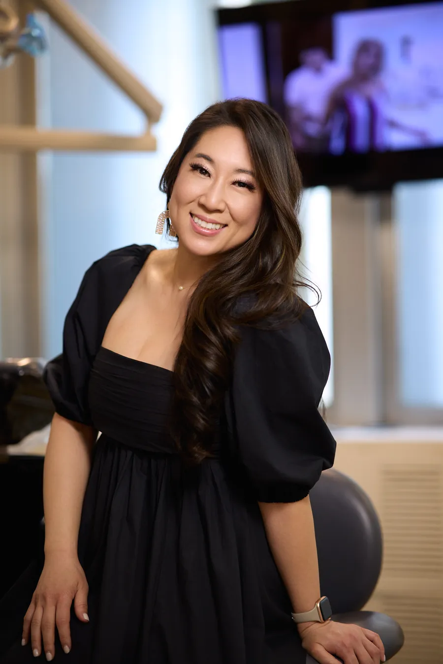Smiling woman in a black dress seated in a dental office, brand portrait