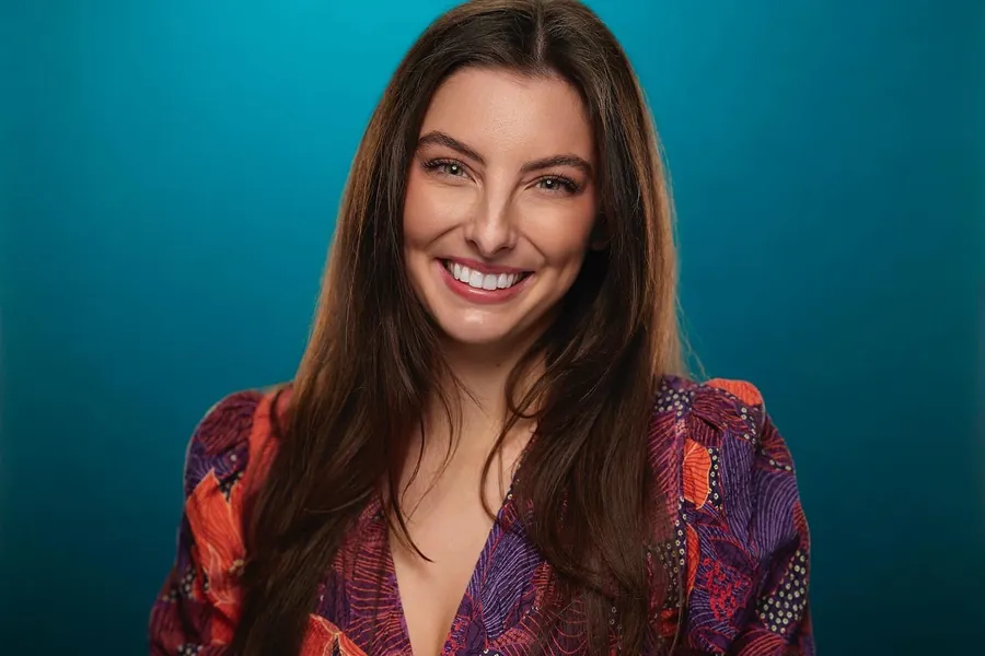 Smiling woman in a patterned top against a teal background, professional headshot