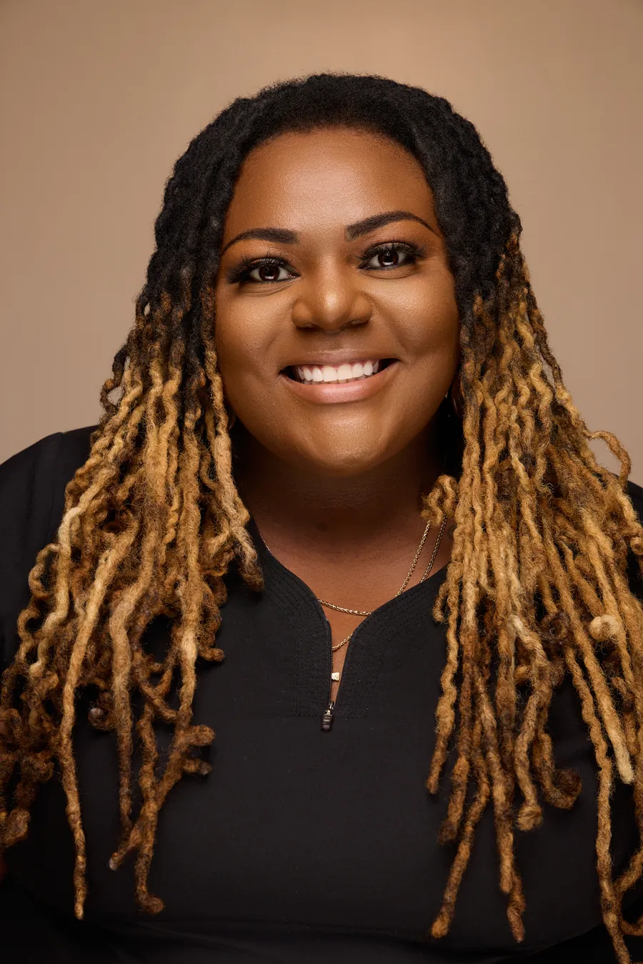 Smiling woman with long braids in a black top against a warm backdrop, team portrait
