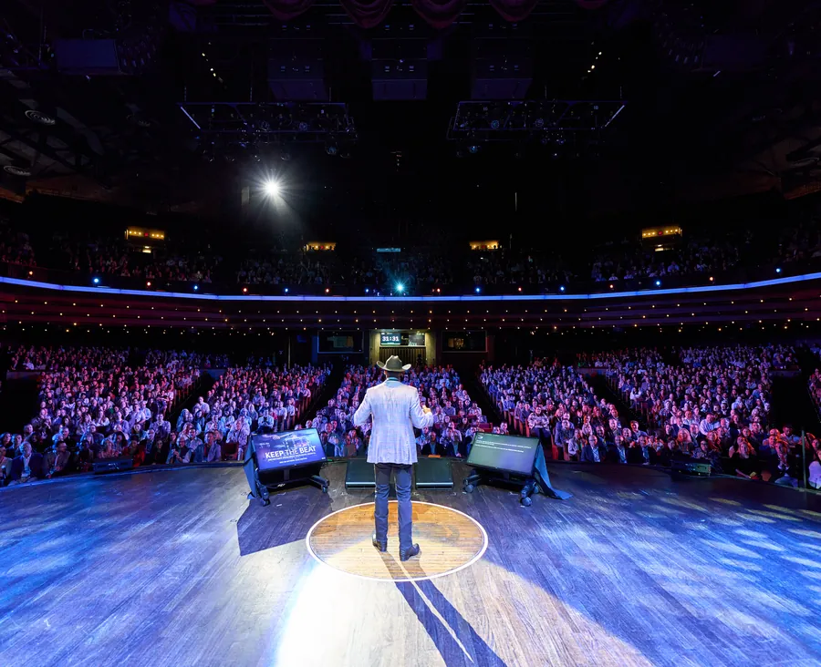 Speaker on a stage in front of a large arena audience at a Nashville corporate conference
