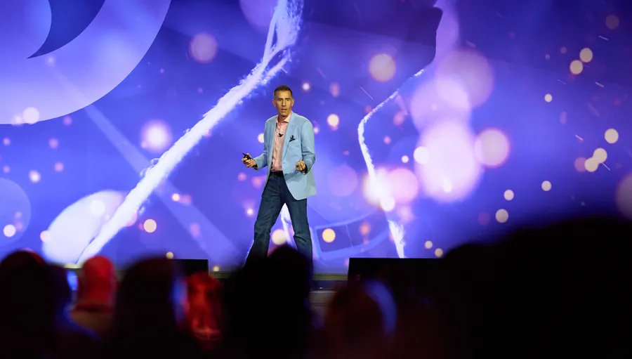Speaker on a stage lit in purple and blue at a corporate event