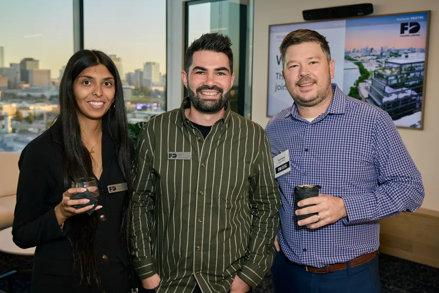 Three guests posing by the window and the Frazier & Deeter screen at the Nashville open house