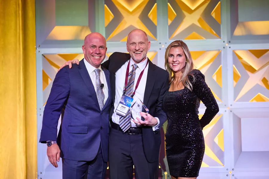 Three people posing on a gold-lit stage at a corporate event