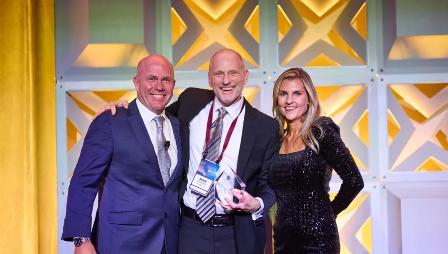 Three people posing on a gold-lit stage at a corporate event