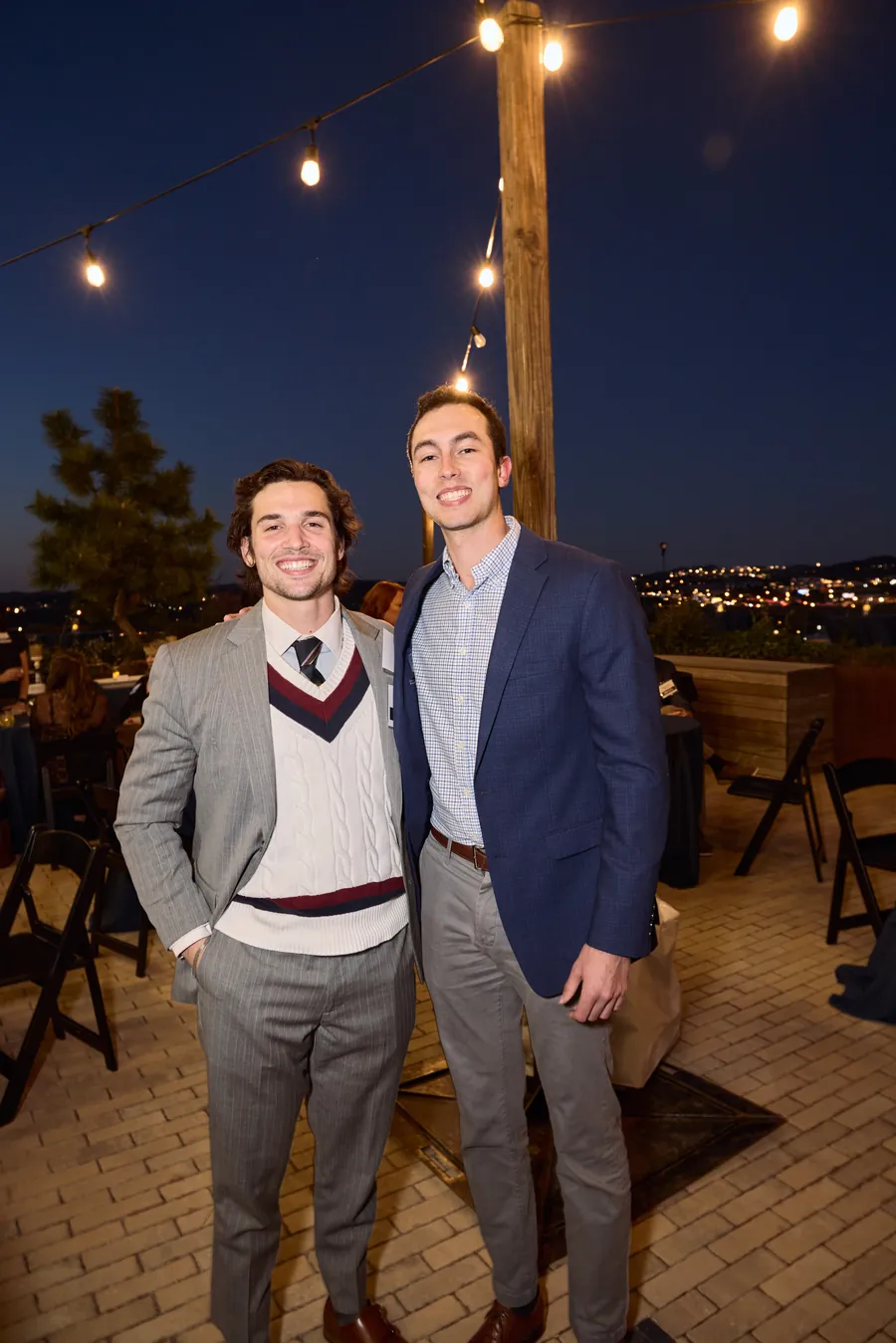 Two men posing on the rooftop with the city lights behind them, Frazier & Deeter open house