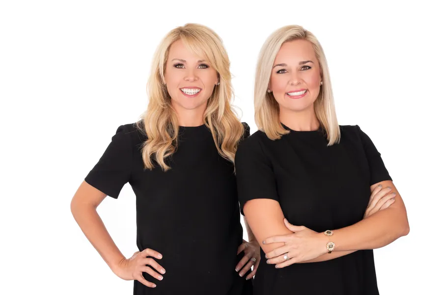 Two women in black tops smiling together against a white backdrop, corporate headshot session