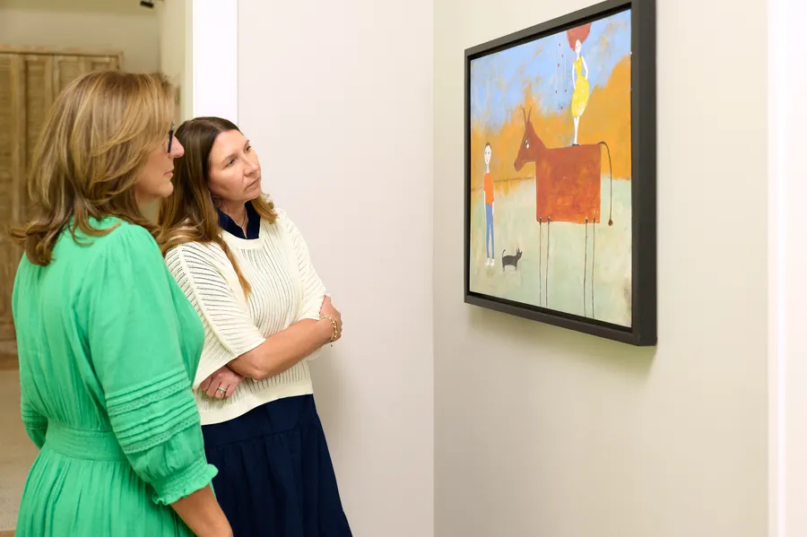 Two women viewing a framed painting on a gallery wall with an art consultant