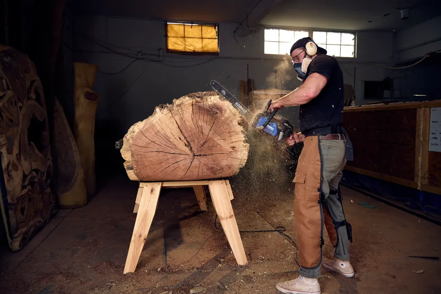 Wide shot of a woodworker cutting a log with a chainsaw in the workshop