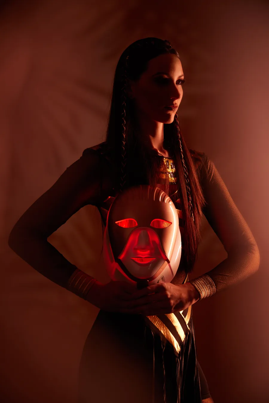 Woman in a gold Egyptian-style outfit holding a red glowing mask, Cleopatra Mask launch