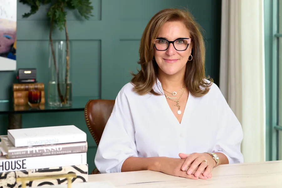 Woman in a white blouse seated at a desk in a styled office, portrait for an art consultant's brand
