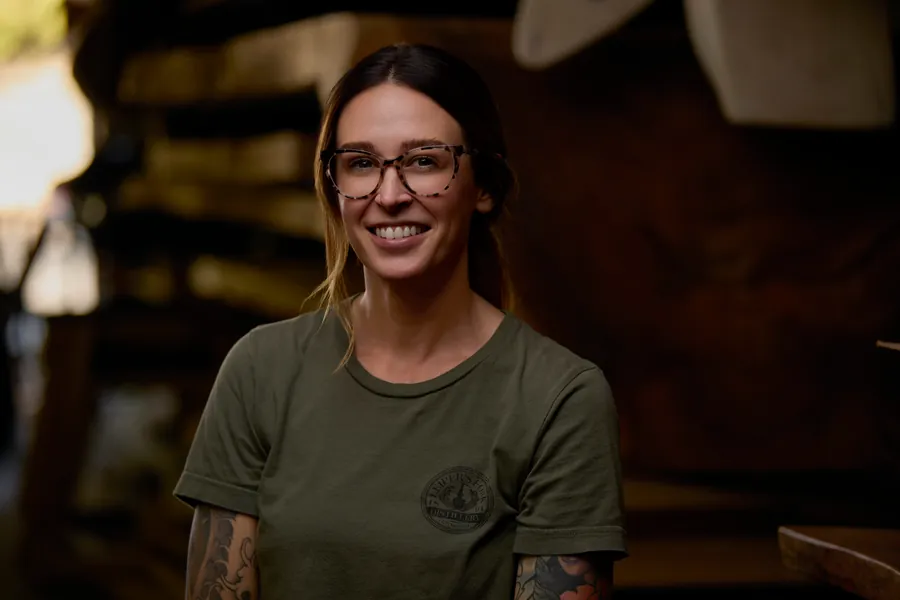 Woman with glasses in an olive t-shirt smiling in the workshop, branding portrait