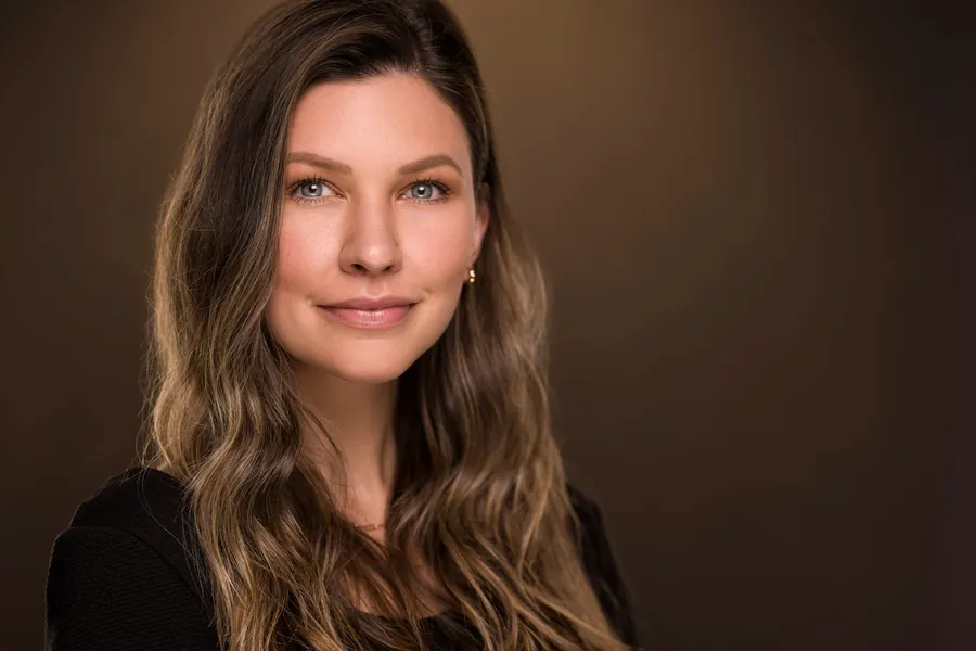 Woman with long brown hair against a warm, dark background, professional headshot