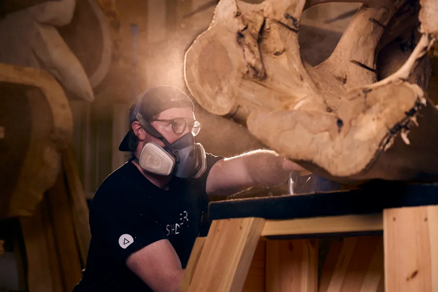 Woodworker in a respirator sanding a large live-edge wood slab, Sawdust & Whiskey branding photo
