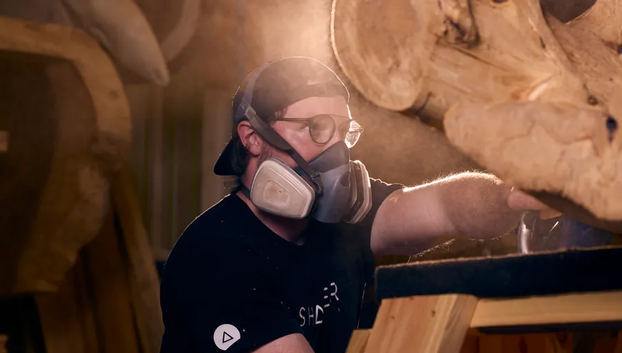 Woodworker in a respirator sanding a large live-edge wood slab, Sawdust & Whiskey branding photo