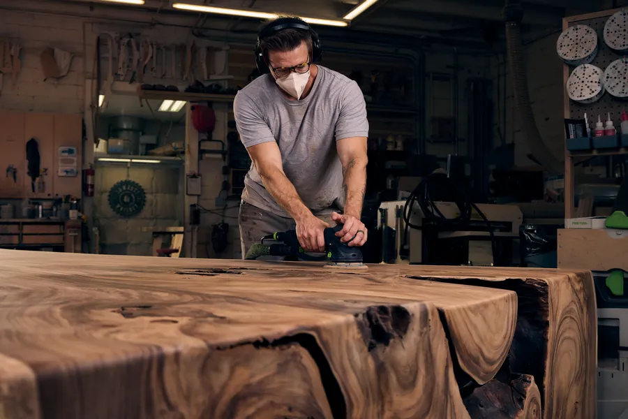 Woodworker sanding a live-edge table in a workshop, branding photography